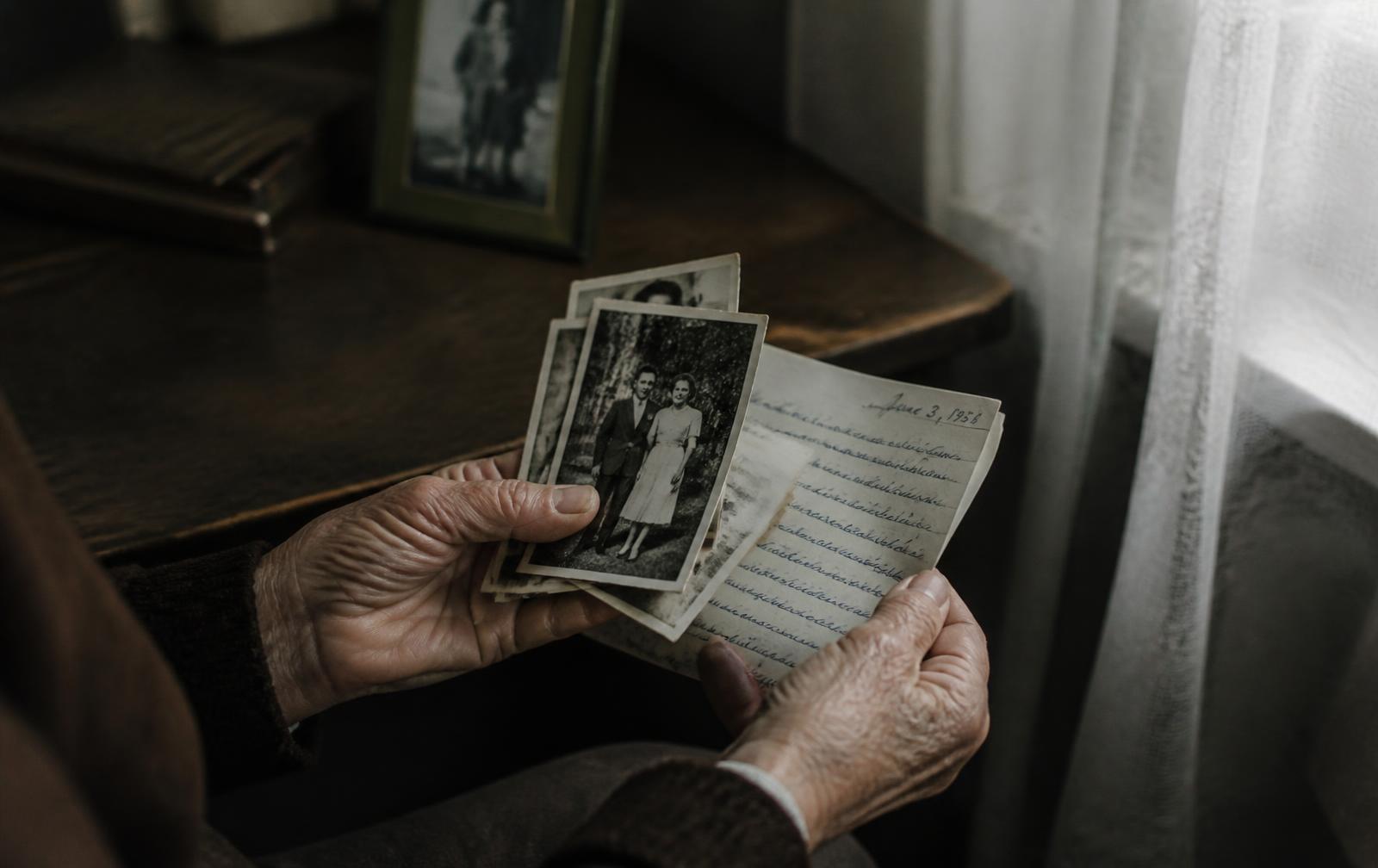 An elderly woman's hands holding faded family photographs and a handwritten letter